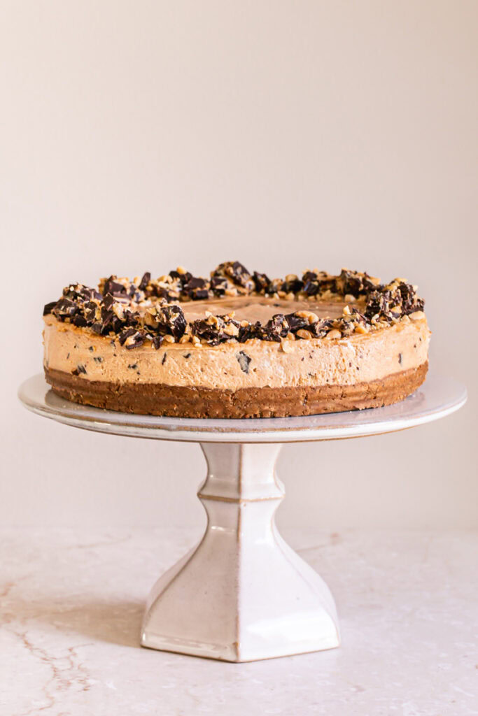 unsliced No-Bake Peanut Butter Cup Pie garnished with chopped peanut butter cups and peanuts on a cake stand