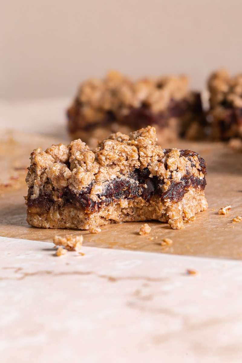 a single Peanut Butter Oat Date Crumb Bar with a bite taken out of it on a piece of parchment paper with more bars behind it