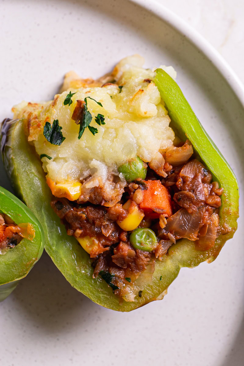 a shepherd's pie stuffed green bell pepper cut in half to reveal the lentil shepherd's pie filling topped with mashed potatoes