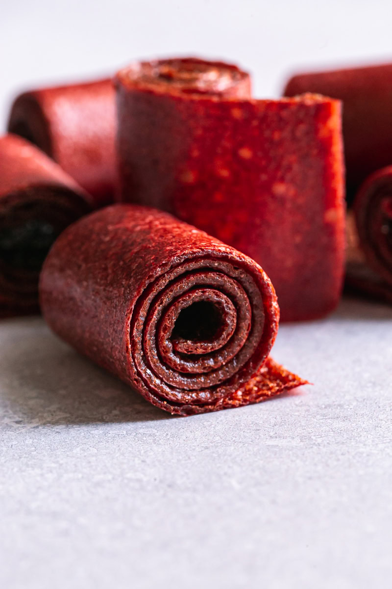 close up of a rolled up strawberry mango fruit roll up with others rolled up in the background