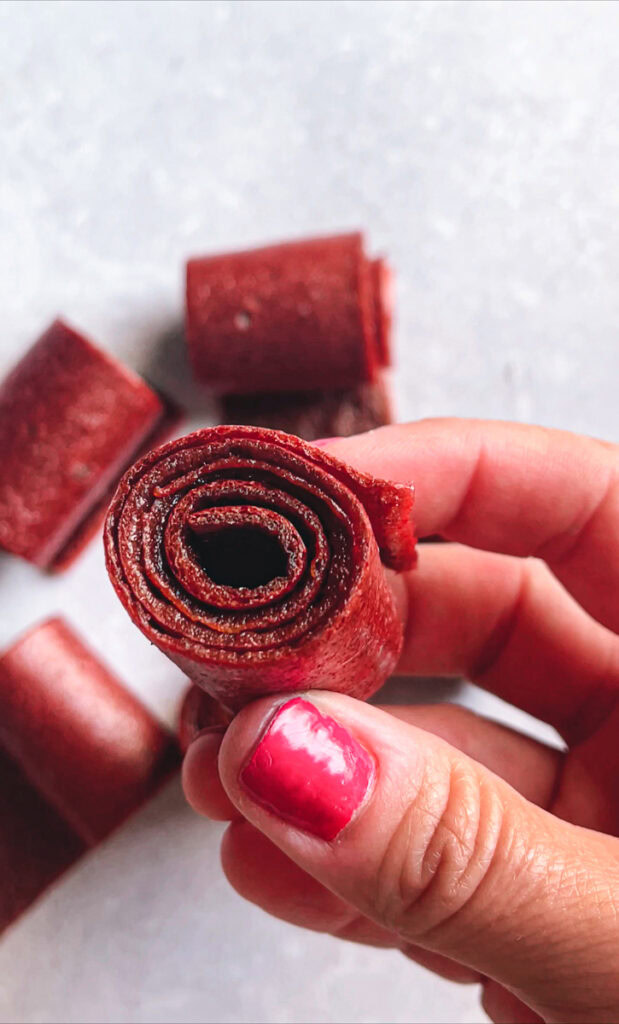 hand holding a Strawberry Mango Fruit Leather (Fruit Roll-Ups) rolled up