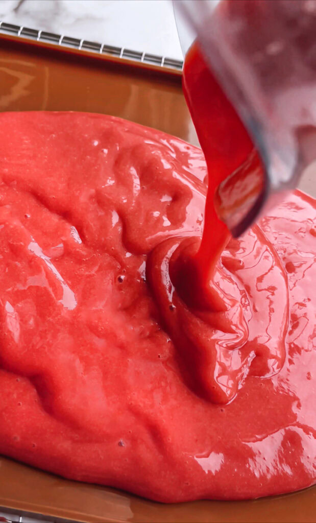 action shot of pouring the blended strawberries and mango out onto a silicone baking mat