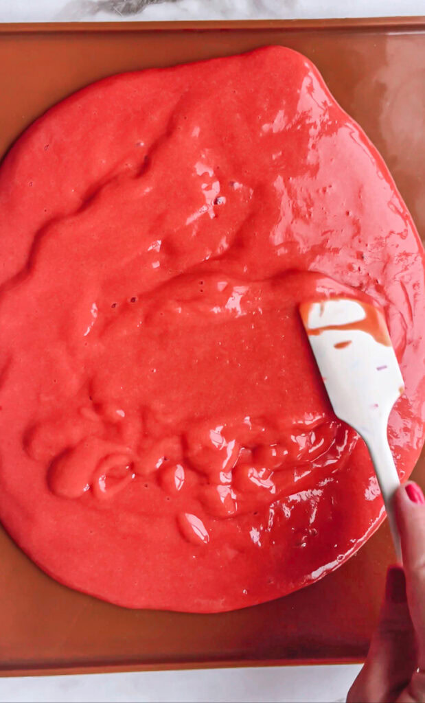 action shot of spreading the strawberry mango mixture out on the silicone baking mat