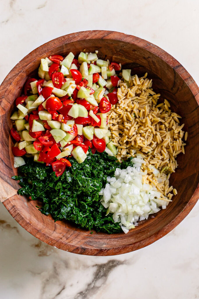 gluten free chickpea orzo, finely diced parsley, diced cucumber and tomato and diced onion in a wooden salad bowl, unmixed