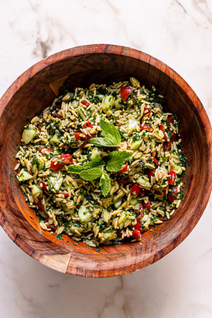gluten-free Tabouli Orzo Salad garnished with fresh mint leaves in a wooden bowl