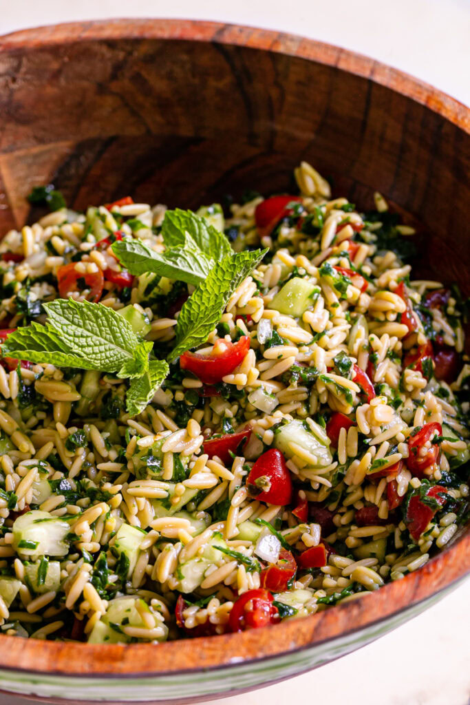 3/4 close up of gluten-free Tabouli Orzo Salad garnished with fresh mint leaves in a wooden bowl