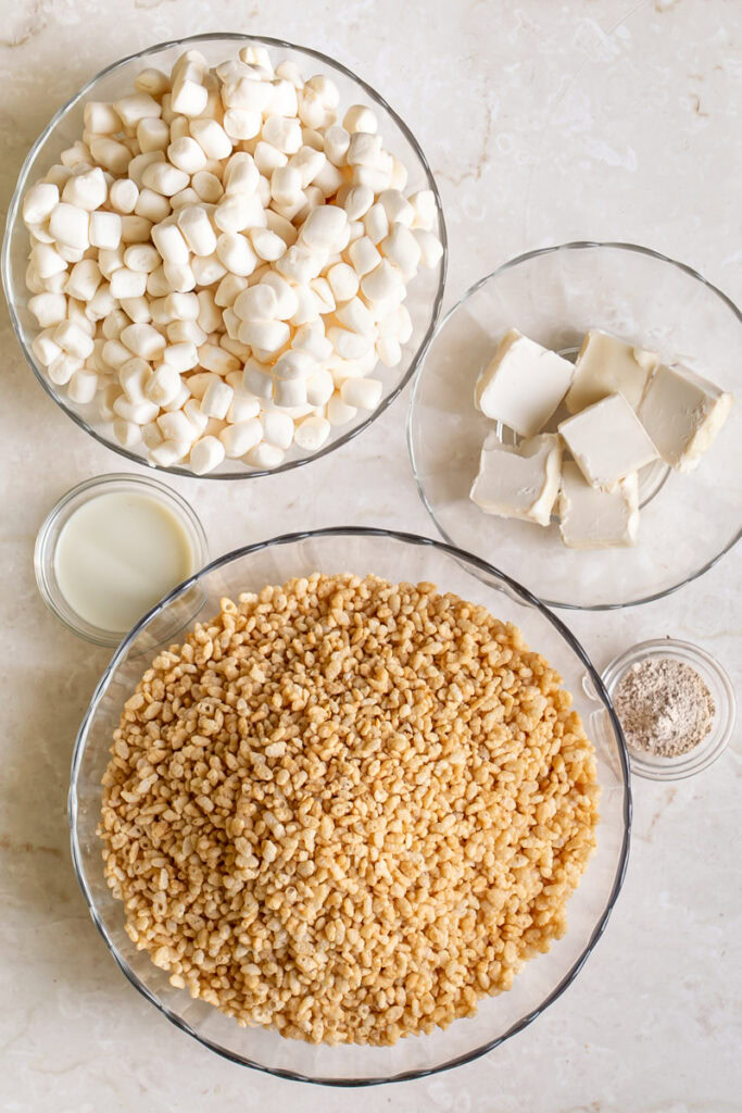 All of the ingredients used to make these vegan chai Rice Krispie treats- a bowl of vegan marshmallows, brown Rice Krispies, vegan butter, plant milk, and chai spice