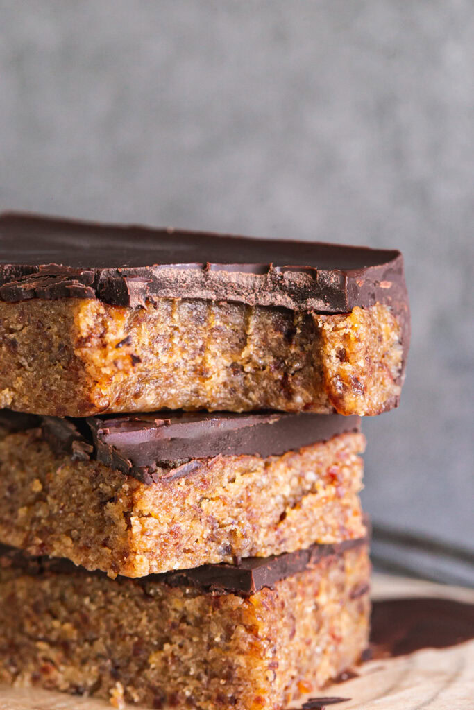 a close up of three almond flour date cookie dough bars stacked on top of one another, the top one with a bite taken out of it