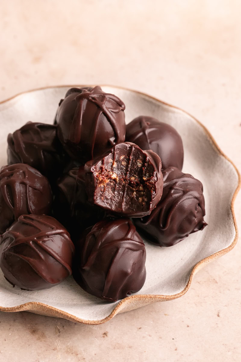 a plate of chocolate crunch date truffles piled on top of one another, one with a bite taken out of it