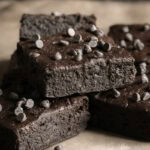 fudgy flourless date brownies stacked on top of one another topped with mini chocolate chips.
