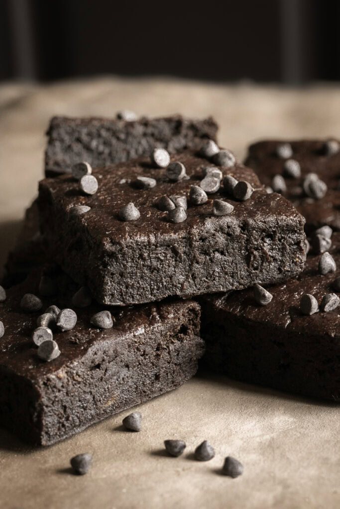 fudgy flourless date brownies stacked on top of one another topped with mini chocolate chips.
