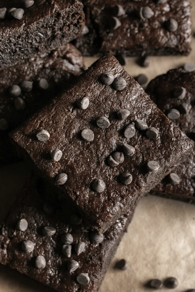 close up overhead shot of fudgy flourless date brownies stacked on top of one another topped with mini chocolate chips.