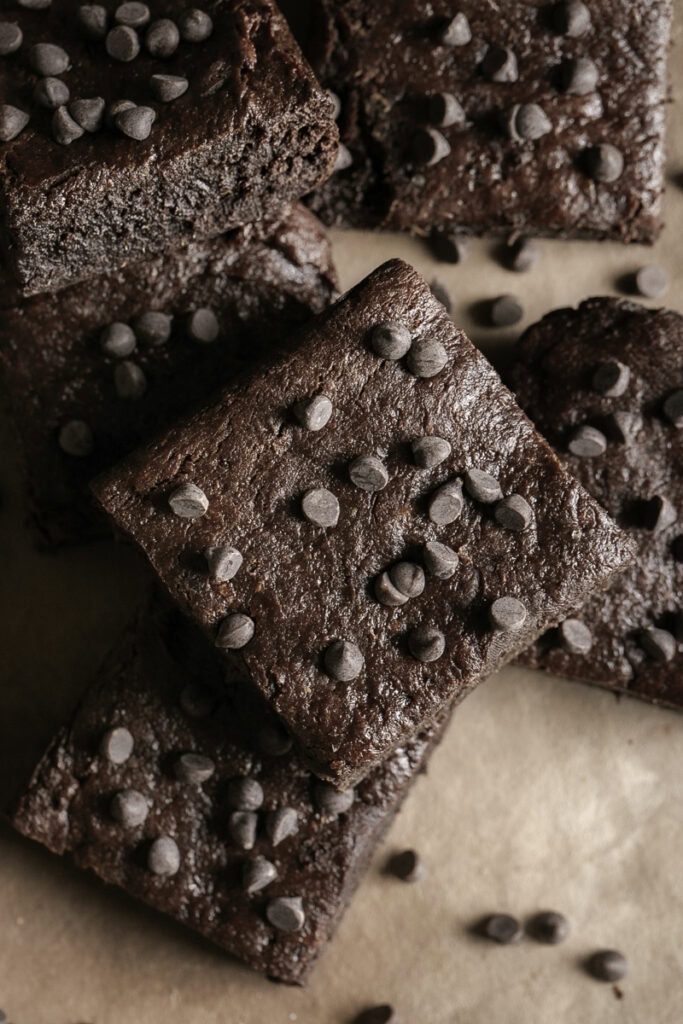 overhead shot of fudgy flourless date brownies stacked on top of one another topped with mini chocolate chips.