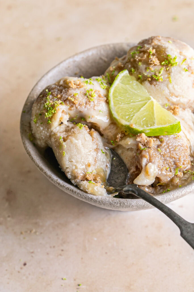 3/4 image of 3 scoops of No-Churn Key Lime Pie Ice Cream in a bowl with with a spoonful of ice cream on a spoon 