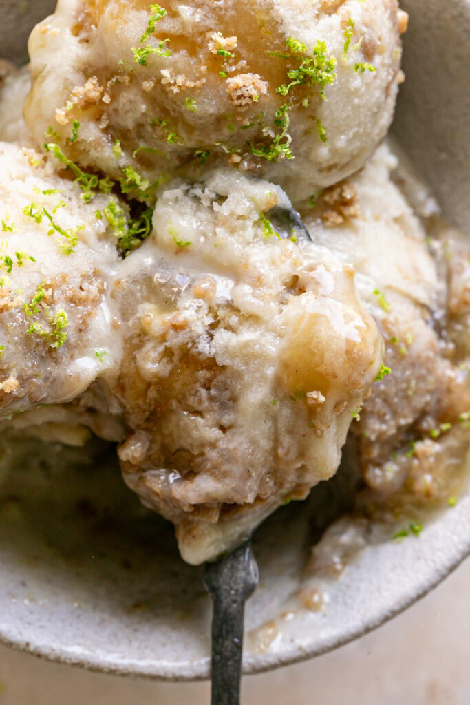 a close up of a spoonful of No-Churn Key Lime Pie Ice Cream in a bowl with 2 other scoops