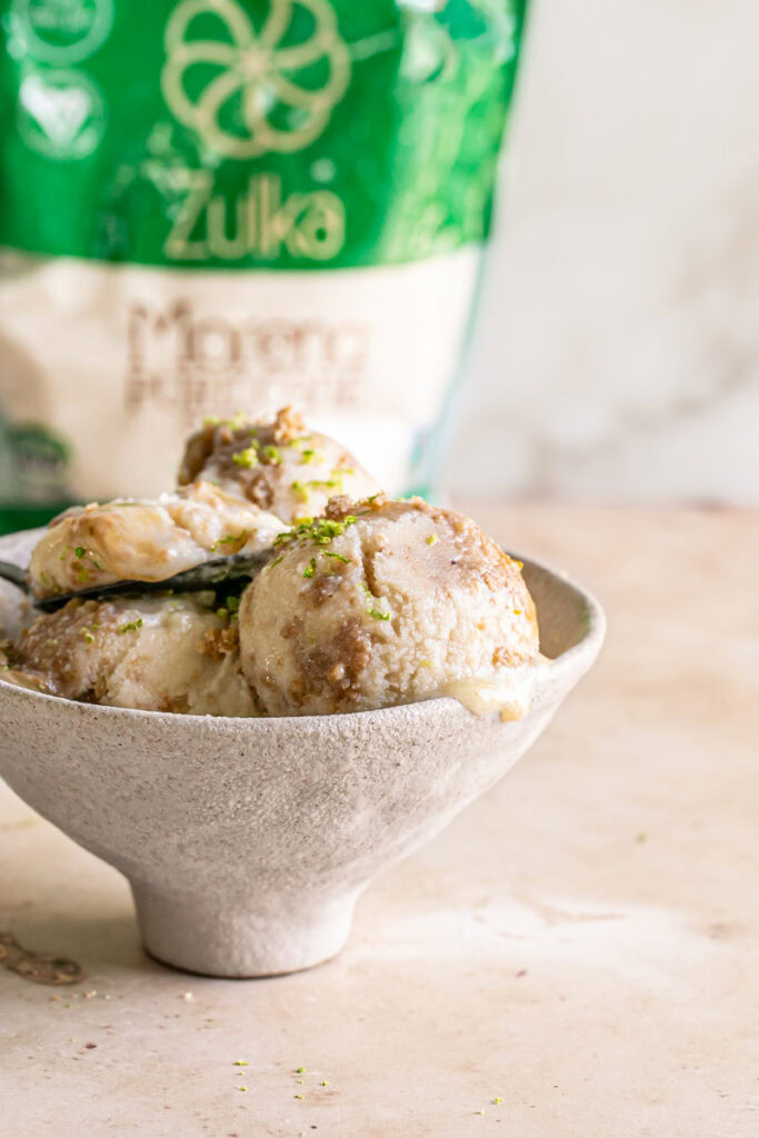 a bowl filled with 3 scoops of No-Churn Key Lime Pie Ice Cream with a spoon in it and a bag of Zulka morena pure cane sugar in the background