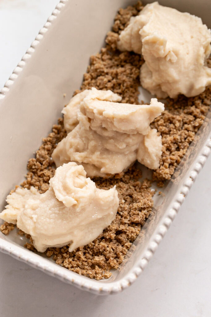 3 scoops of dairy free vanilla ice cream dolloped on top of the almond flour cookie dough crumble in a loaf pan