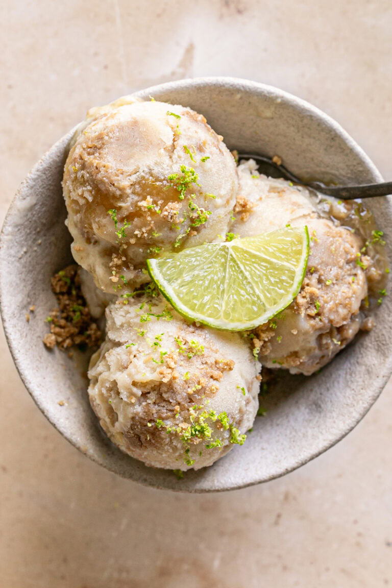 three scoops of No-Churn Key Lime Pie Ice Cream in a bowl garnished with a slice of lime, cookie dough crumble and lime zest