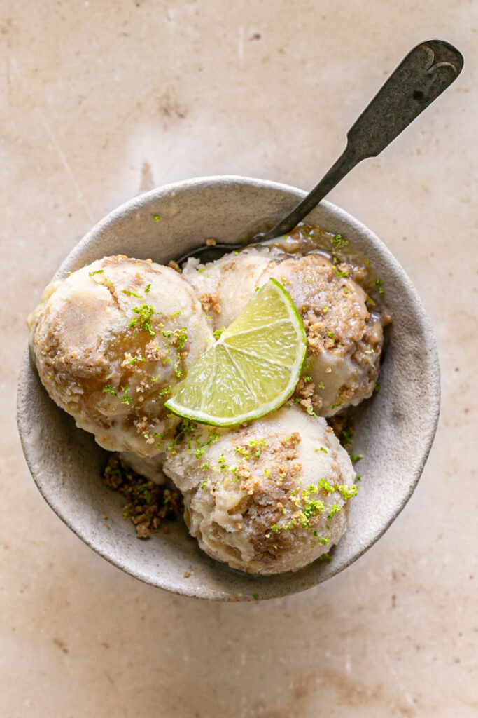 three scoops of No-Churn Key Lime Pie Ice Cream in a bowl garnished with a slice of lime, cookie dough crumble and lime zest