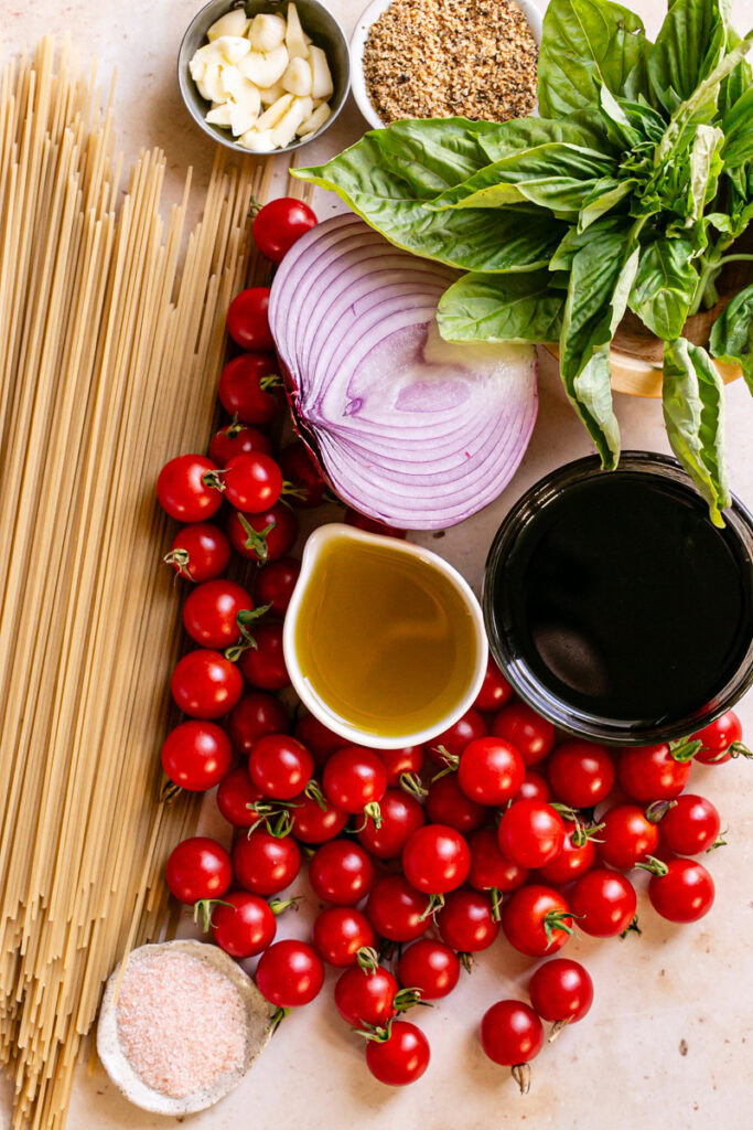 the ingredients used to make this bruschetta pasta: dry noodles, cherry tomatoes, red onion, fresh basil, garlic, olive oil, salt, balsamic vinegar, toasted breadcrumbs