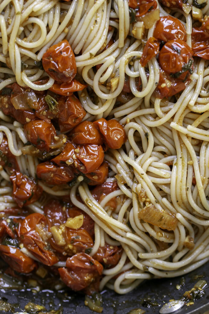 a close up shot of the noodles tossed in with the cherry tomatoes in the skillet.