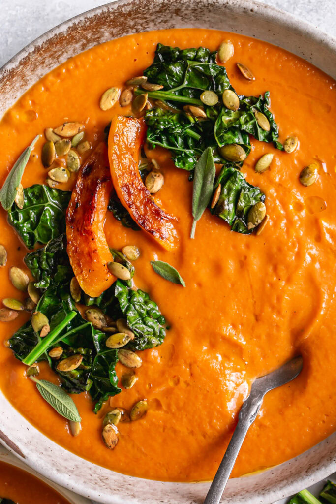 a close up of a bowl of Roasted Butternut Squash Tomato Soup with Crispy Kale and a spoon in the bowl