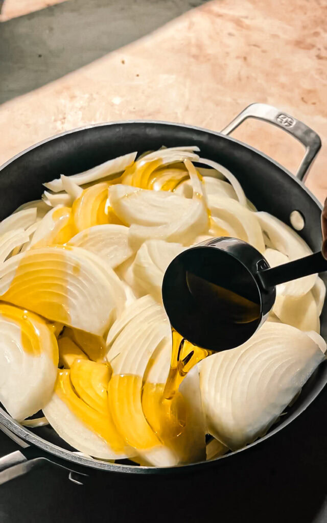 drizzling olive oil over sliced sweet yellow onions in a skillet 