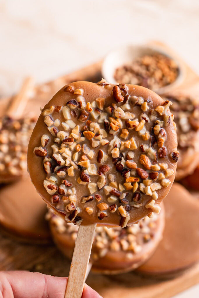 holding a peanut butter caramel apple pop garnished with chopped nuts