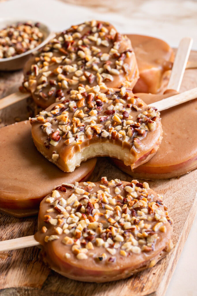 3/4 shot of caramel apple pops stacked on top of one another, one with a bite taken out of it