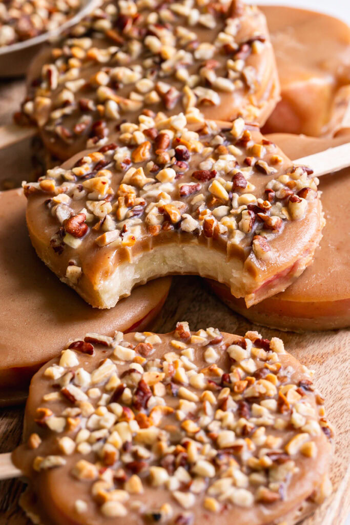 close up of 3/4 shot of caramel apple pops stacked on top of one another, one with a bite taken out of it
