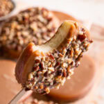 a close up of holding a peanut butter caramel apple pop with a bite taken out of it to see the apple slice on the inside