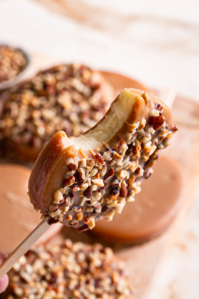 a close up of holding a peanut butter caramel apple pop with a bite taken out of it to see the apple slice on the inside