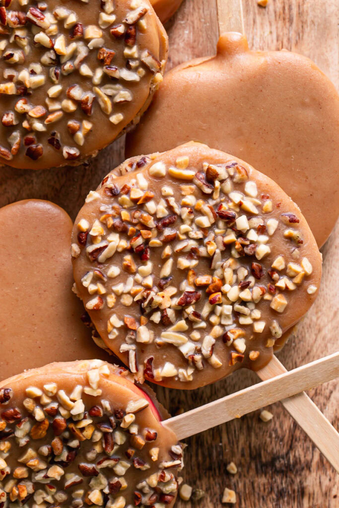 caramel apple slices on popsicle sticks, some garnished with chopped nuts