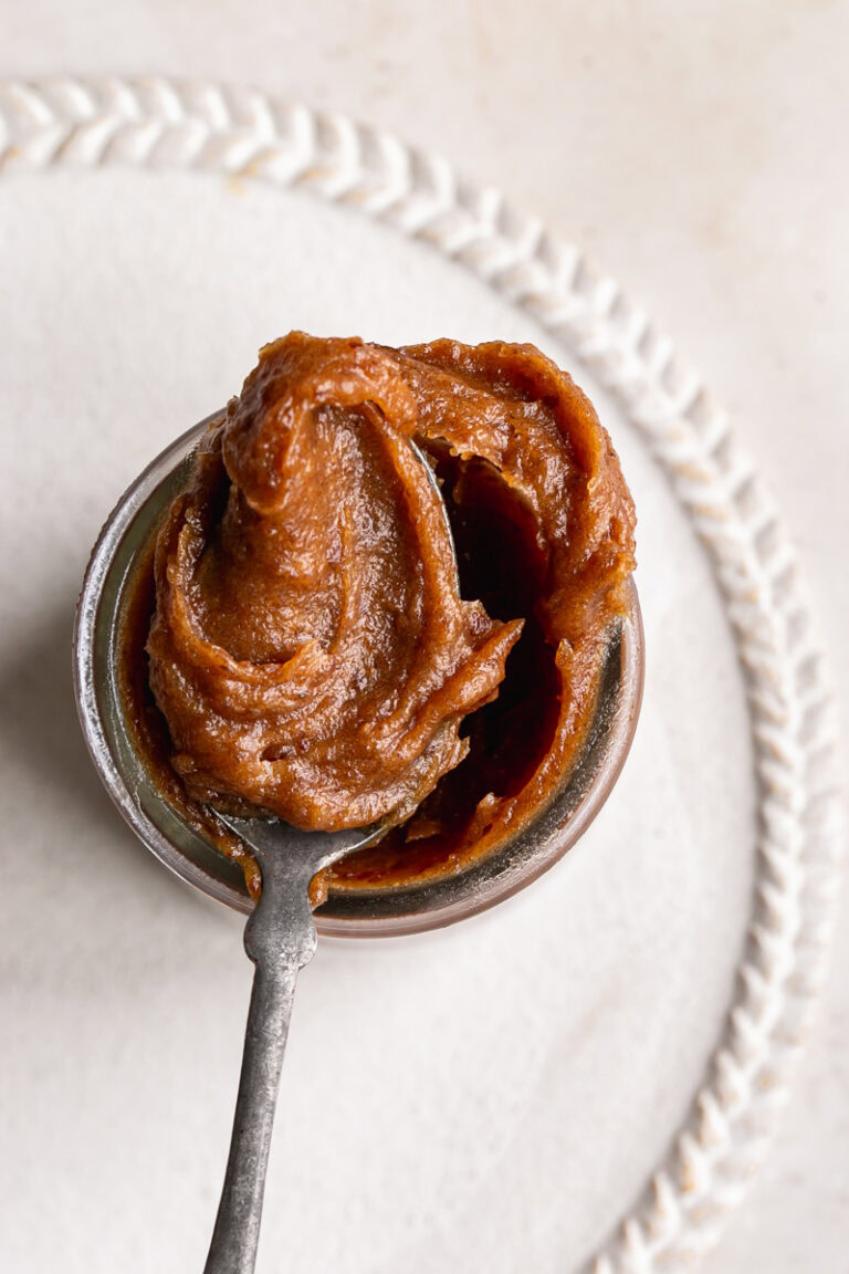 an overhead shot of date caramel in a jar with a scoop of caramel on a spoon resting on the mouth of the jar