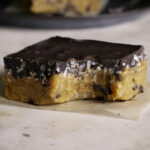 a close up of one Almond Flour Pumpkin Cookie Dough Crunch Bar on a piece of parchment paper, a bite taken out of it