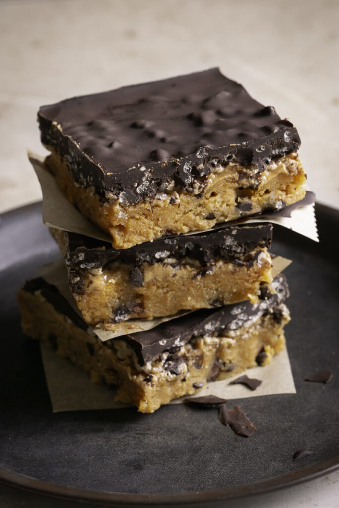 a close up of Three Almond Flour Pumpkin Cookie Dough Crunch Bars stacked on top of one another on a round metal plate 