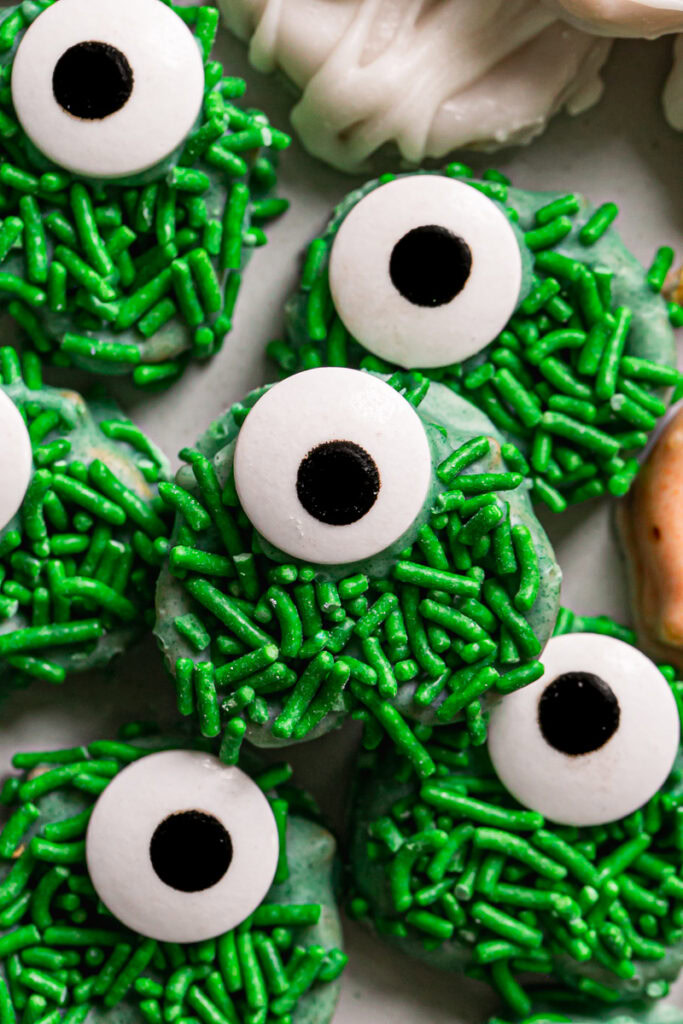 a close up of the a round plate with chocolate covered one eyed green sprinkle covered pretzel monsters