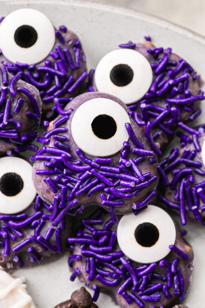 a close up of the a round plate with chocolate covered one eyed purple sprinkle covered pretzel monsters