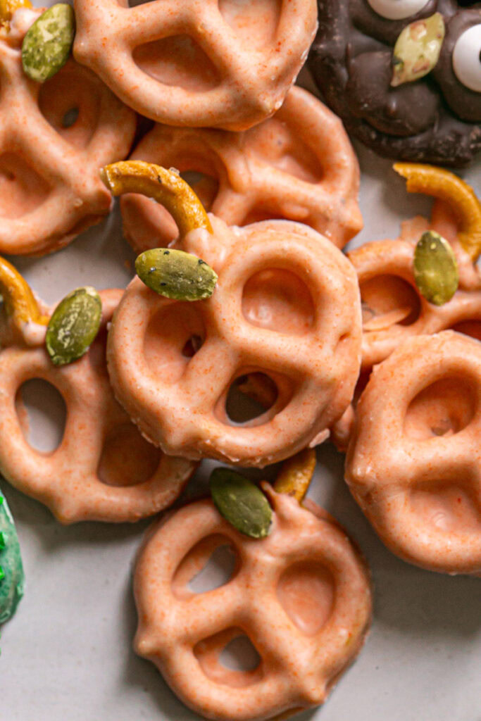 orange colored white chocolate covered pretzel pumpkins with a pretzel stem and a pumpkin seed leaf