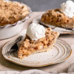 a slice of healthy dutch apple pie with a scoop of vanilla ice cream on top and the rest of the pie in the pie plate in the background