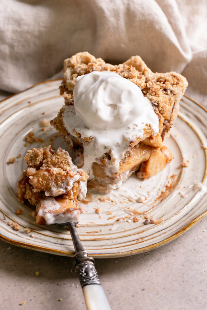 a slice of apple pie on a plate topped with melting vanilla ice cream and a forkful of pie
