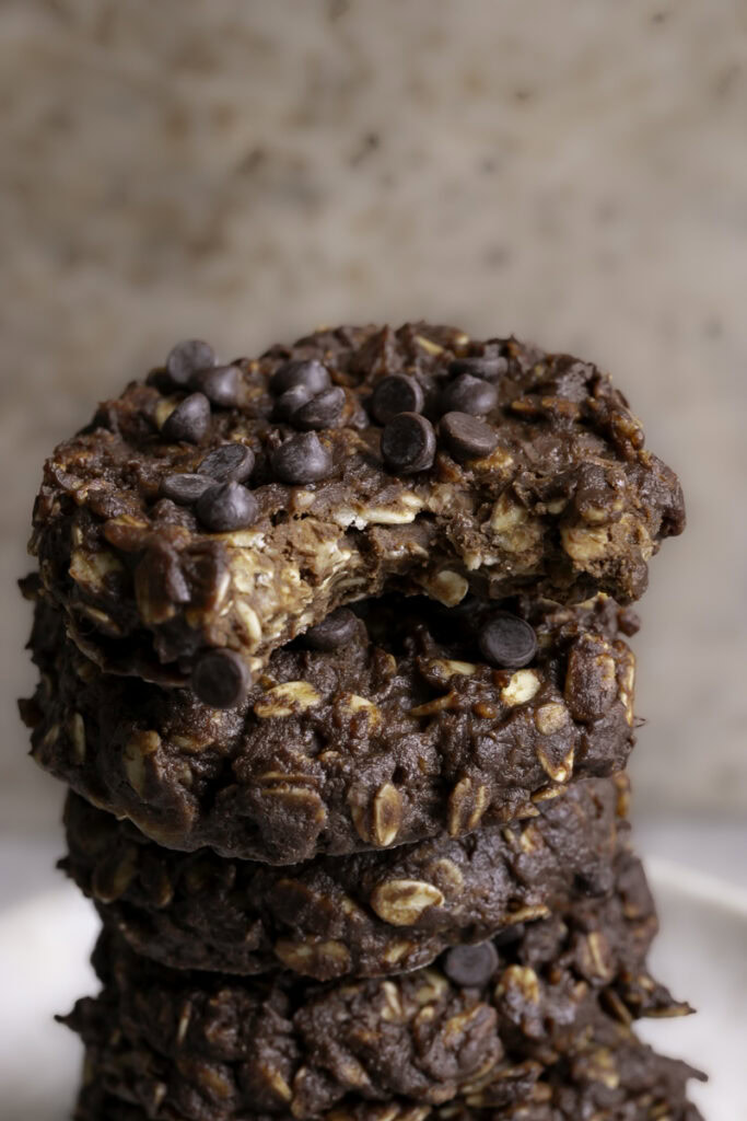 a close up of no-bake pumpkin brownie oatmeal cookies stacked on top of one another, the top one with a bite taken out of it
