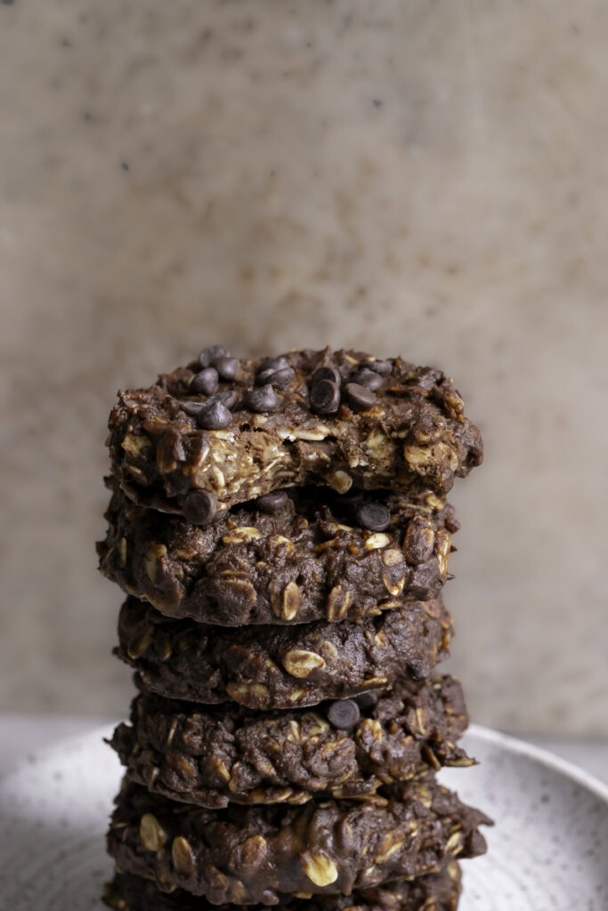 no-bake pumpkin brownie oatmeal cookies stacked on top of one another, the top one with a bite taken out of it