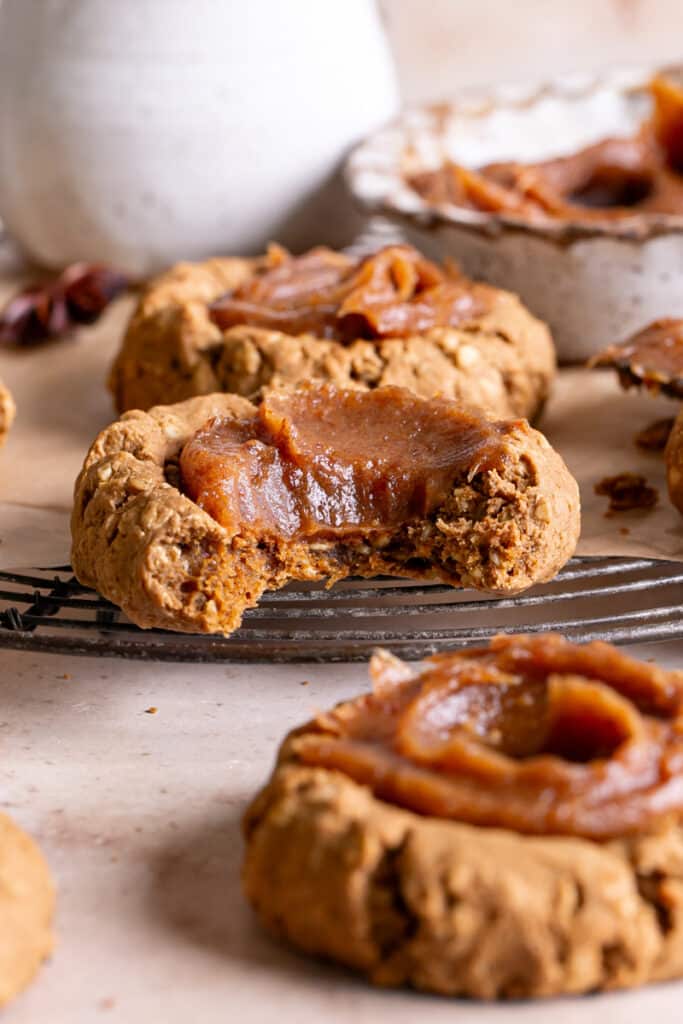 a close up of Pumpkin Spice Oatmeal Thumbprint Cookies with Date Caramel, one with a bite taken out of it