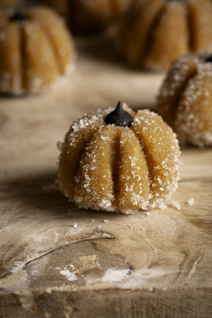 close up of Sugared Almond Flour Pumpkin Cookie Dough bite shaped like a pumpkin and topped with a chocolate chip for the stem