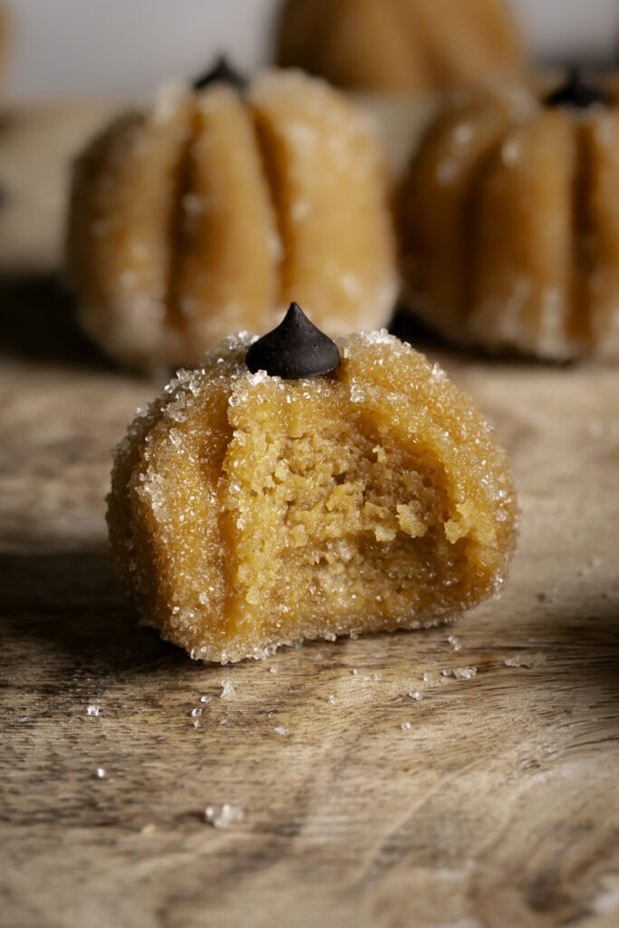 a close up of a Sugared Almond Flour Pumpkin Cookie Dough on a wooden cutting board with a bite taken out of it