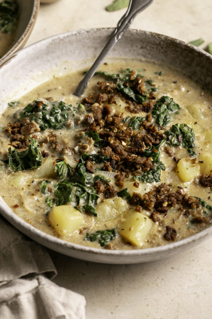 3/4 close up of a bowl of vegan zuppa toscana soup with a spoon in the bowl