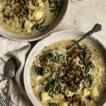 two bowls of vegan zuppa toscana soup, a linen napkin and a spoon in one of the bowls