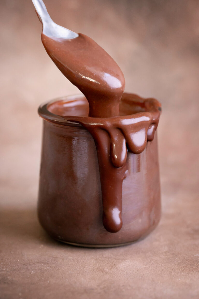 a jar of healthy vegan hot fudge, oozing over the side with a spoon scooping some hot fudge out.