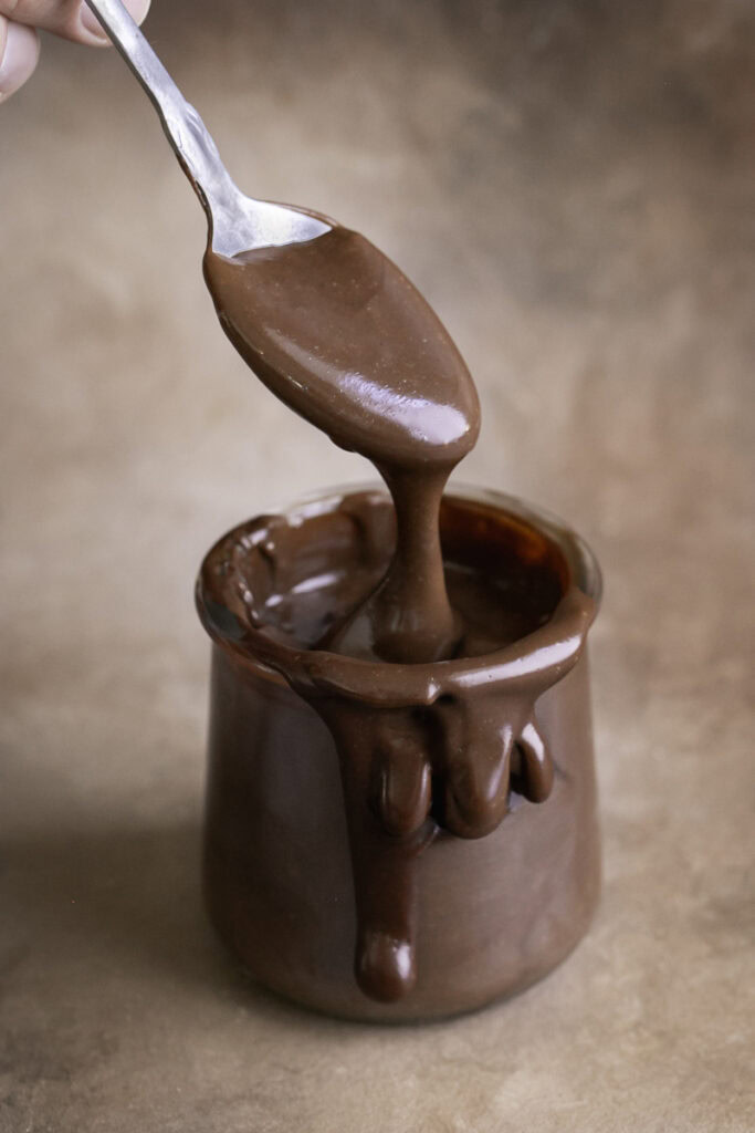 a jar of healthy vegan hot fudge, oozing over the side with a spoon scooping some hot fudge out.